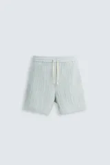 Bermuda negra de corte regular, confeccionada en tejido jacquard con efecto arrugado. Presenta cintura elástica ajustable con cordón blanco, bolsillos laterales y bolsillos traseros de vivo.