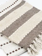 Pie de cama rectangular de algodón con diseño a rayas horizontales en tonos beige y marrón, con flecos en los extremos.