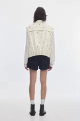 Chaleco oversize de denim color crudo con estampado de lunares negros, cuello camisero, bolsillos delanteros y cierre frontal de botones metálicos.