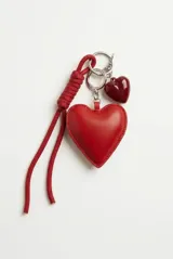 Llavero rojo con argolla metálica, cordón trenzado de tela y dos dijes en forma de corazón, uno grande acolchado de cuero sintético y uno pequeño brillante.
