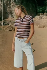 Bermuda tipo jorts de denim en color celeste claro, con tiro medio, diseño de cinco bolsillos y cinturilla doblada. Presenta roturas decorativas en la parte delantera y cierre frontal con cremallera y botón metálico.