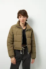 Campera puffer corta color verde oliva, de nylon, con cuello alto, bolsillos laterales con cierre y cordones ajustables en la cintura.