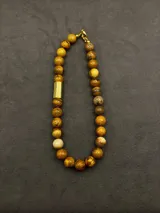 Collar de cuentas de piedras naturales en tonos tierra, con detalles de tubos dorados en los laterales.