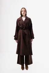 Trench de algodón color marrón chocolate, con solapas amplias, cierre cruzado con botones y cinturón ajustable a la cintura. Presenta mangas largas con trabillas en los puños y un corte holgado de largo midi.