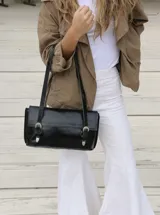 Cartera de hombro combinada en cuero liso marrón oscuro y cuero con pelo vacuno estampado tipo animal print. Presenta solapa frontal con dos correas decorativas con hebillas metálicas y detalles de herrajes en bronce.