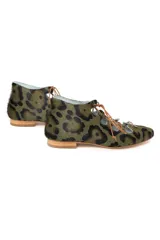 Semibotín de piel de pony con estampado animal print en tonos verde y marrón. Presenta un diseño con aberturas laterales onduladas, cierre de cordones finos y punta afilada. Cuenta con suela de cuero y cuña interna.
