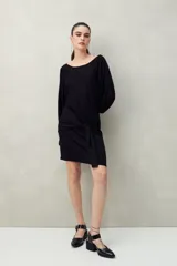 Vestido corto de punto color negro, con mangas largas y amplias, escote bote y detalle de lazo anudado en la cintura. Presenta una textura con sutil brillo integrado.