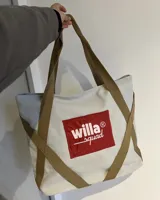 Bolso tote de lona color beige con asas de cinta marrón. Estampado frontal con el logo "Willa Squad" en rojo y blanco.