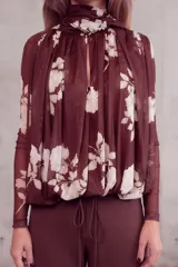 Camisa bordó de manga larga en tejido translúcido, con estampado floral en tonos claros y un pañuelo o echarpe integrado al cuello que cae sobre el frente.