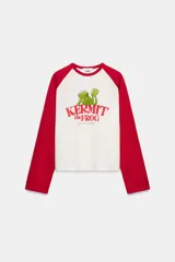 Camiseta de manga larga con cuello redondo, corte regular fit. Color blanco con mangas raglán rojas. Estampado frontal de Kermit the Frog y el texto "Kermit the Frog" en rojo.