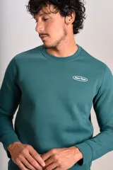 Buzo verde oscuro de cuello redondo, mangas largas con puños elásticos y pequeño estampado ovalado en el pecho.
