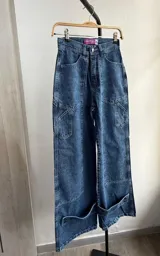 Pantalón de jean azul con efecto lavado, corte wide leg, bolsillos laterales y detalle de botones en el ruedo.
