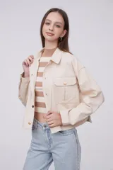 Chaqueta de algodón color beige, con diseño holgado, cuello tipo camisa, cierre frontal con botones metálicos y bolsillos frontales con solapa.