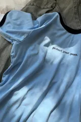 Remera blanca de algodón con cuello redondo y manga corta. Presenta un texto bordado en el centro del pecho que dice "enjoy the now.".