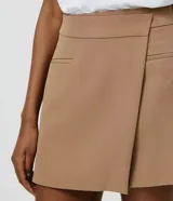 Short pollera de sastrería color rosado, con diseño asimétrico superpuesto en el frente, bolsillos ribeteados decorativos y cierre lateral discreto.