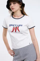 Remera baby blanca de manga corta, con ribetes en contraste azul marino en el cuello y las mangas. Cuenta con un diseño estampado al frente que incluye la leyenda 'SPICY LIFE' y gráficos de ajíes rojos.