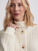 Cárdigan largo color crema, confeccionado en tejido de punto acanalado de viscosa. Tiene corte relajado, cierre frontal con botones y bolsillos de parche.