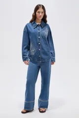Sobrecamisa de jean azul medio, de corte oversize, con mangas largas y detalles de tachas decorativas en la parte frontal y trasera.