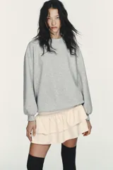 Vestido corto que combina una parte superior tipo sudadera gris de manga larga con puños, y una falda corta de volantes color crema. La parte superior es de tejido de punto jaspeado y la falda tiene dos capas de volantes.