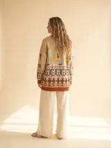 Cardigan de tejido grueso con cuello shawl, estampado tribal en tonos rojo arcilla, crema y negro, con cierre frontal de botones y puños en tono kontrastante.