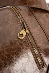 Mochila de cuero sintético marrón con efecto craquelado, asa superior y placa metálica frontal con el logo de la marca.