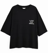 Remera negra de corte oversize con cuello redondo y mangas cortas. Presenta un estampado tipográfico en color blanco en el lado izquierdo del pecho con la frase 'it's NOT THAT SERIOUS'.