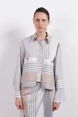 Camisa corta de algodón y seda con silueta recta, diseño a rayas verticales en tonos gris, blanco y beige, cuello camisero, cierre frontal con botones, mangas largas con puños abotonados, bolsillos de parche con botón a presión en el pecho y bajo recto.