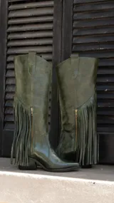 Botas de caña alta confeccionadas en cuero vacuno, con forro interior de cuero, taco cuadrado de 5.5 cm y suela de goma. Presentan un diseño con flecos laterales y cierre metálico.