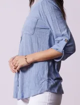 Blusa Ninety color beige con textura, cuello base con escote en V y abertura central con botones. Tiene un bolsillo en el pecho y mangas 3/4 regulables con presilla y botón.