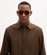 Camisa de corte comfort en color marrón con diseño de rayas verticales finas. Presenta cuello inglés, cierre frontal abotonado y mangas largas con puños. Confeccionada en una mezcla de liocel y lino.