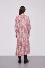 Vestido midi de viscosa con estampado patchwork en tonos rosados y violetas. Presenta cuello redondo con cordones ajustables, mangas 3/4 abullonadas y diseño holgado con falda de volados.