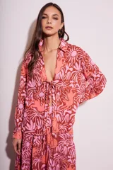 Blusa de poliéster con estampado de flores y animales en tonos rosa y marrón. Tiene cuello camisero, mangas largas y cierre frontal con lazo.