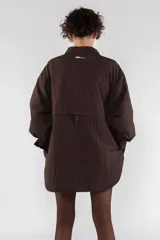 Camisa acolchada marrón con cuello clásico, cierre frontal con botones, manga larga raglán, puños abotonados, bolsillo utilitario en el pecho, bolsillos laterales y canesú abotonado en la espalda.