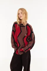 Sweater de punto con diseño geométrico en zigzag, combinando franjas en color marrón, rojo y negro. Presenta cuello redondo, mangas largas y un corte holgado.