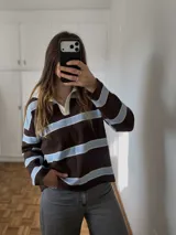 Sweater de tejido bremer doble a rayas horizontales marrones y celestes, con cuello polo y solapa en color blanco, de manga larga y calce holgado.