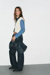 Chaqueta de punto de manga larga con cuello solapa y cierre frontal de botones. Presenta un diseño de bloques de color: cuerpo principal color crema, manga izquierda negra, manga derecha azul claro y cuello negro. Incluye detalles de costura expuesta en azul claro en el cuello y el bajo.