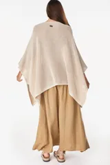 Blusa de punto estilo poncho en color beige, con diseño amplio, cuello redondo y aplique de etiqueta con el logo de la marca en el borde inferior.