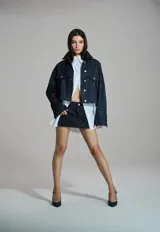 Chaqueta de jean estilo glam con acabado brillante, de corte cropped, con bolsillos frontales con solapa y cierre de botones metálicos.