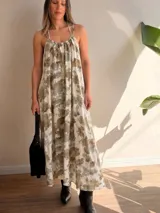 Vestido largo de silueta amplia y caída fluida, confeccionado en modal con estampado floral en tonos neutros. Cuenta con escote fruncido, tiritas finas ajustables al cuello y elástico en la espalda. Incluye forro corto interno y pequeño tajo en la espalda.