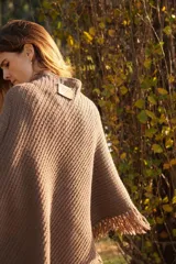 Poncho tejido en lana merino color marrón, con diseño de punto acanalado y terminación con flecos en el borde inferior. Incluye una pequeña etiqueta de cuero en la parte posterior.