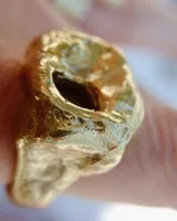 Anillo dorado con forma irregular y un agujero en el centro.