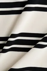 Remera de corte holgado en punto de algodón pesado con diseño a rayas horizontales negras y fondo blanco, cuello redondo acanalado en contraste, hombros caídos y mangas tres cuartos amplias.