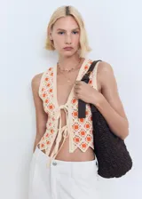 Top de crochet color crudo con flores naranjas, sin mangas, con escote en V y cierre frontal con lazos.