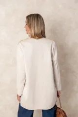 Chaqueta larga color beige con diseño abierto, cuello redondo y mangas largas. Presenta detalles bordados artesanales con aplicaciones de cuentas y toques dorados en la zona de los hombros.