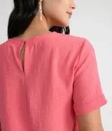 Blusa blanca de poliéster con cuello redondo, mangas cortas, cierre trasero en forma de gota, pequeñas aberturas laterales y acabados en pespuntes en las mangas y el cuello.