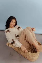 Sweater color crema tejido en lana merino con cuello redondo y mangas largas. Presenta diseño de llamas marrones con detalles en zigzag negros.