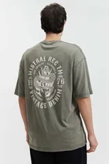 Remera oversize de algodón con efecto acid wash, color blanco hueso. Estampado grande en la espalda con un diseño circular que incluye una serpiente enroscada, texto "MISTRAL REG", "LOS ANGELES", "CALIFORNIA", "VINTAGE DENIM", "REGISTERED" y "TM 76".