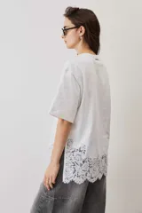 Remera blanca de algodón, de corte oversize, manga corta y cuello redondo, con detalle de aplique de encaje floral en el borde inferior.