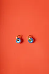 Aros tipo argolla dorados con dije circular esmaltado en colores rojo, azul, verde y blanco, con un patrón floral.