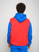 Canguro de felpa Umbro del Club Nacional de Football, con diseño tricolor en rojo, azul y blanco. Presenta capucha con cordones ajustables, bolsillo tipo canguro frontal, logo de la marca y escudo del club bordados en el pecho.